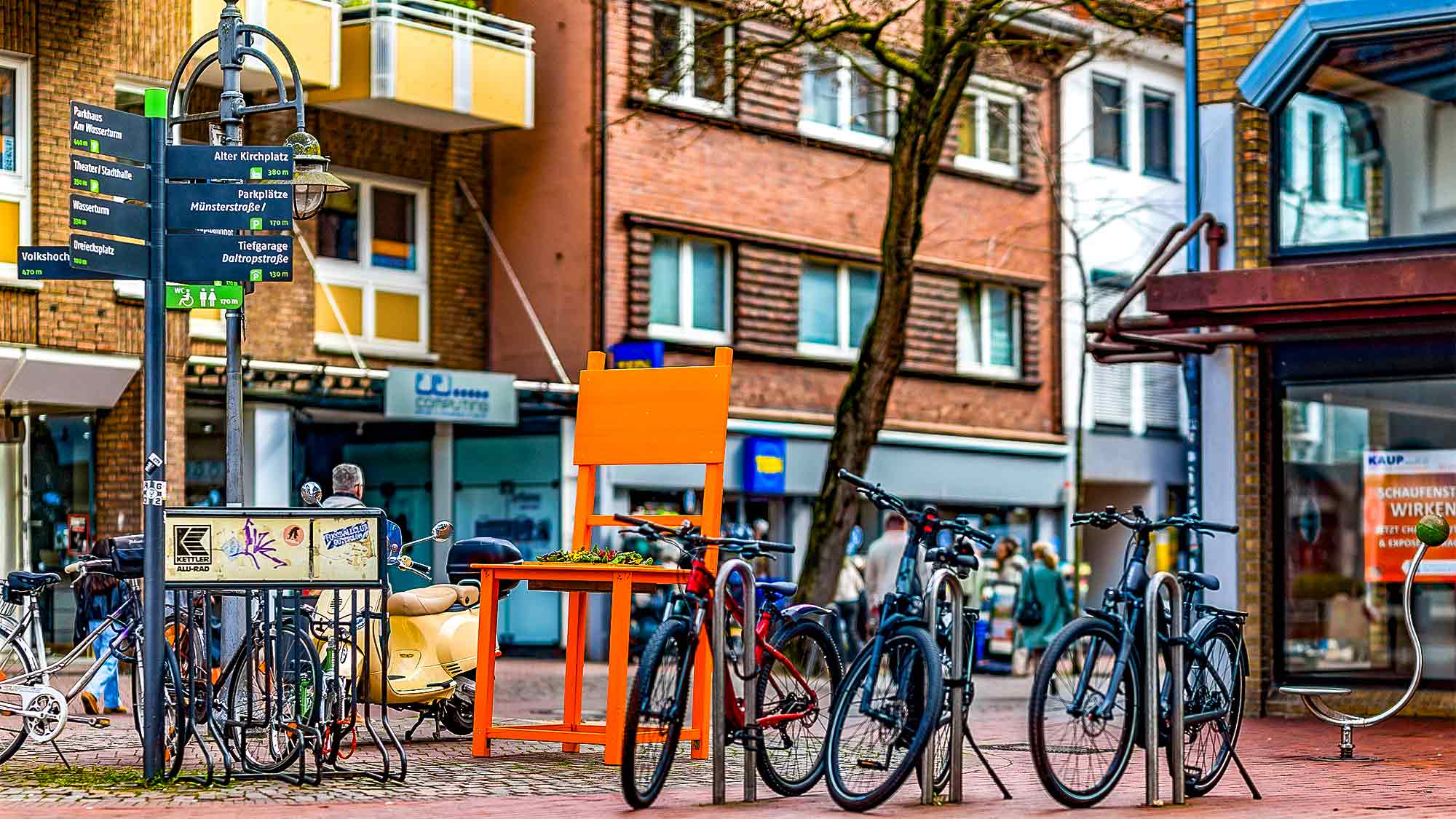 NOW Commons: &raquo;Gütersloher Frühling 2026&laquo;, Orange Chair mit Veilchen, Fußgängerzone Königstraße Gütersloh